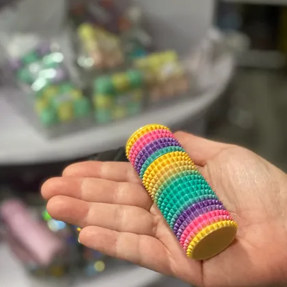 A hand holding a stack of colorful spiky rainbow clicker fidget toys at Mindspace Toys.