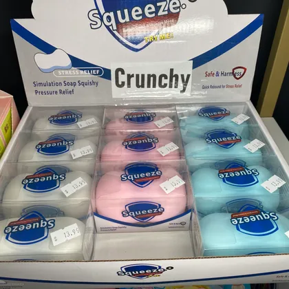 Display box of Squeeze brand crunchy stress-relief squishy toys in pink, white, and blue at Mindspace Toys.