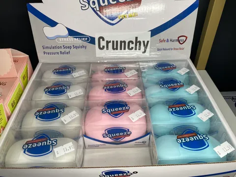 Display box of Squeeze brand crunchy stress-relief squishy toys in pink, white, and blue at Mindspace Toys.